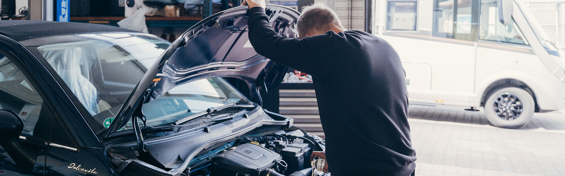 Ein Mechaniker sprüht Kriechöl in die Verschlussmechank des Motordeckels
